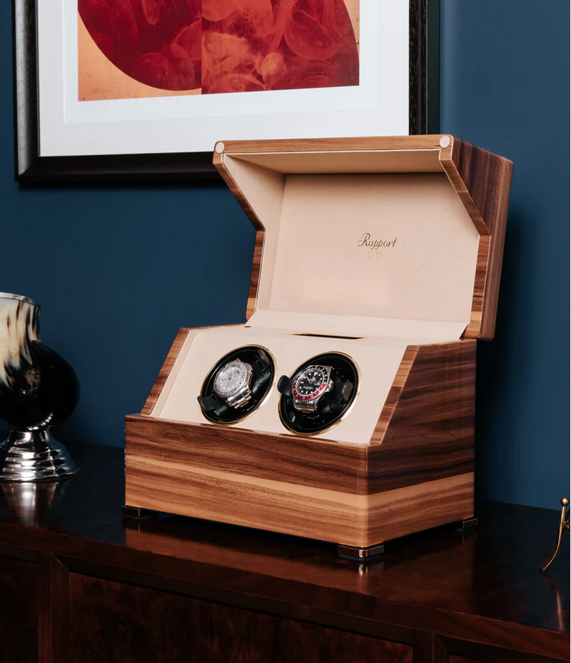 Rapport London Wooden watch box with two watches on a dark surface against a blue wall.
